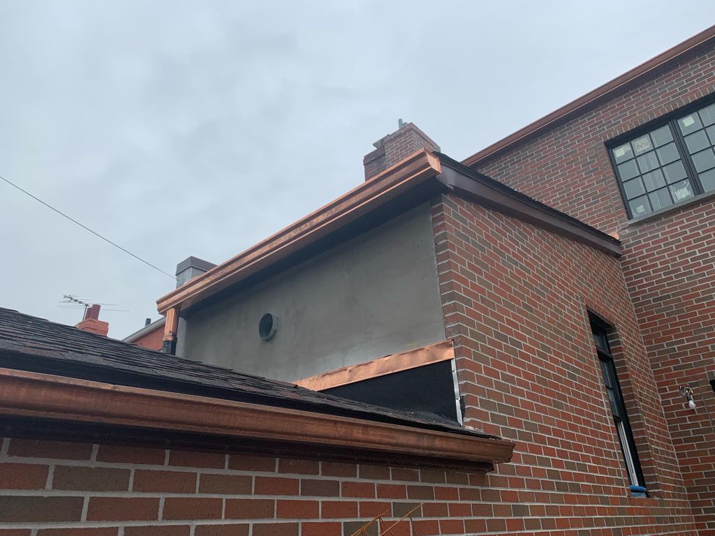 Copper gutter installation with downspout on brick building